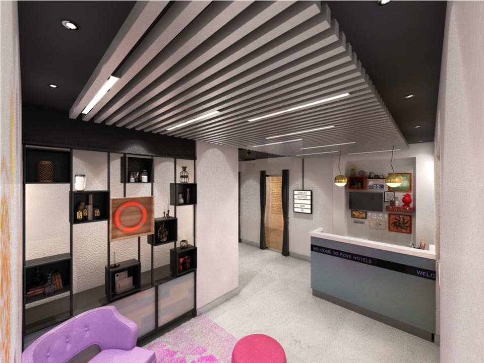 Refurbished mall common-area concierge zone with a black slatted baffle ceiling, recessed and linear LED lighting, polished light-grey stone flooring, a modular black display shelving wall, a dark reception desk with pendant lights, and accent seating in purple and pink.